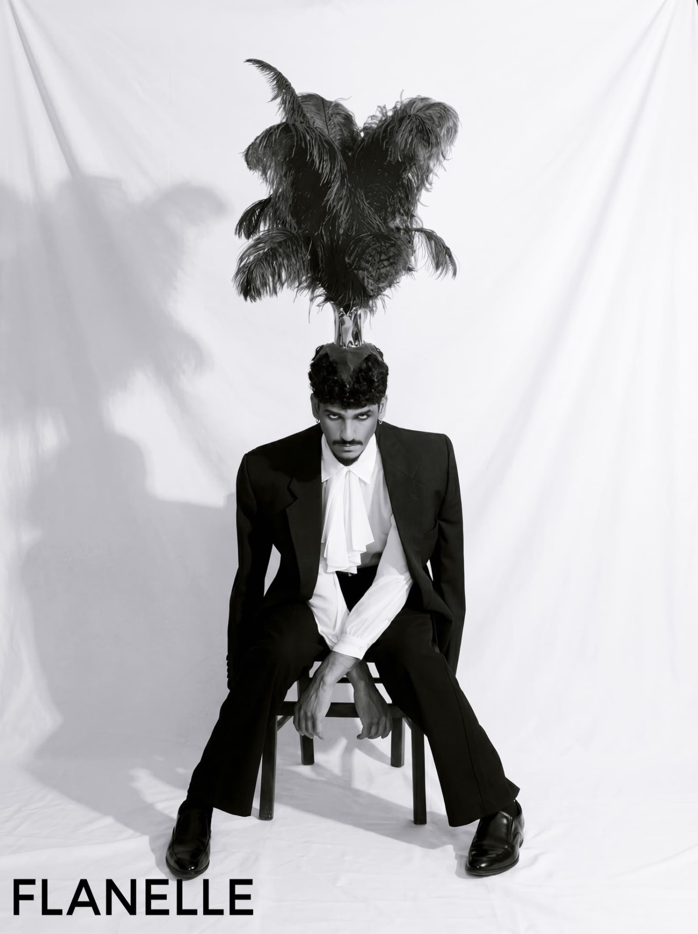 FLANELLE — seated figure in a black suit beneath a tall feather headpiece