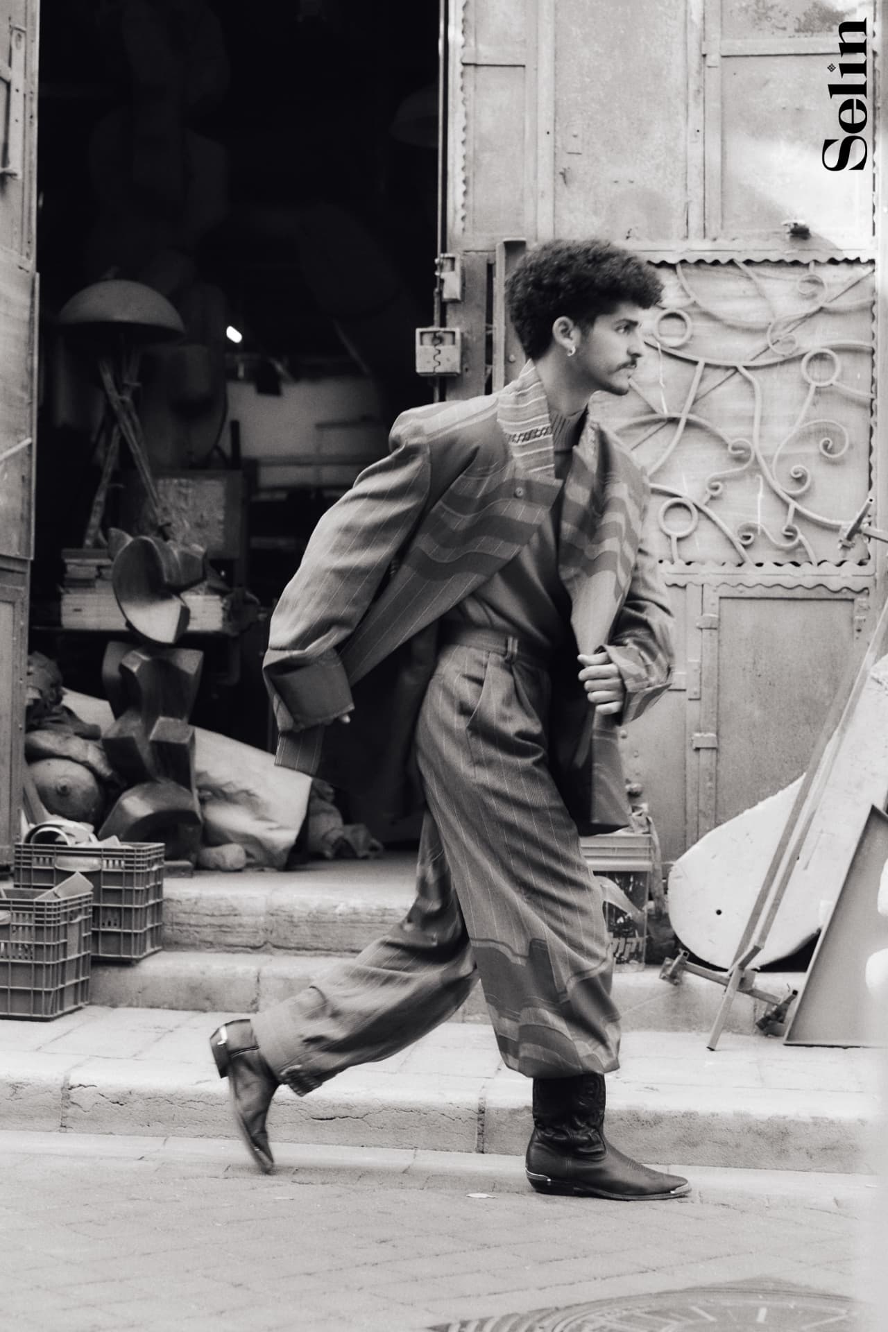 SELIN — model mid-stride past a workshop doorway in an oversized striped suit