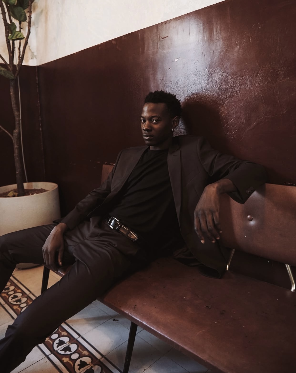 MANTRA — model in a dark suit seated against an oxblood wall