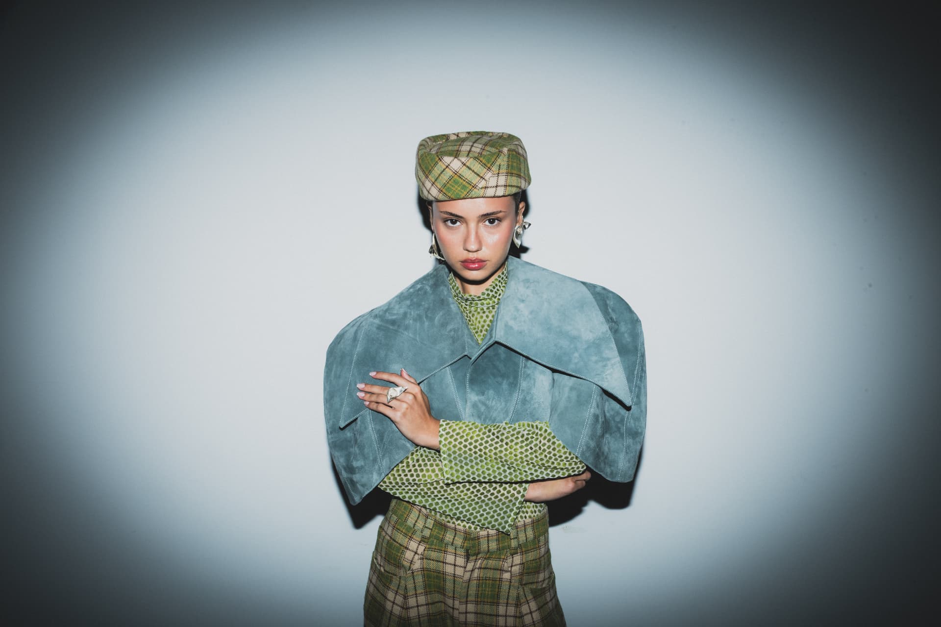 Shenkar BTS 2026 — model in a plaid cap and structured suede cape